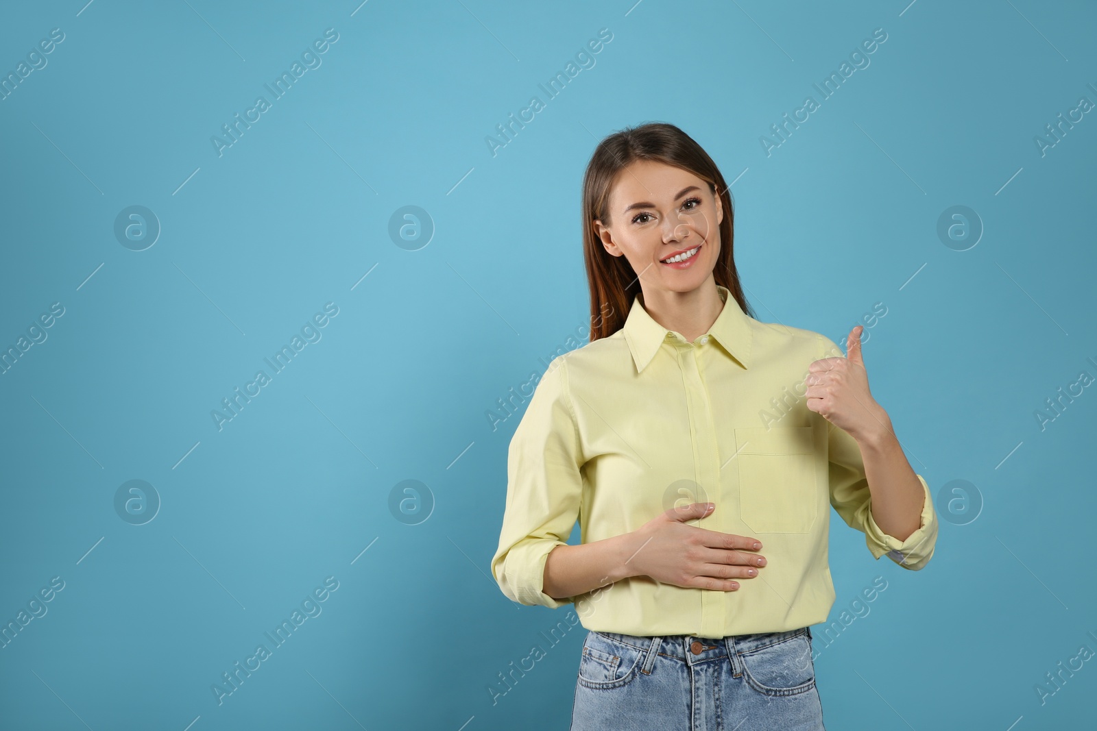 Photo of Healthy woman holding hand on belly and showing thumbs up gesture against light blue background. Space for text