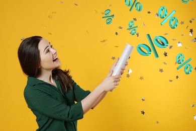Image of Discount offer. Happy young woman blowing up party popper on golden background. Confetti and percent signs in air