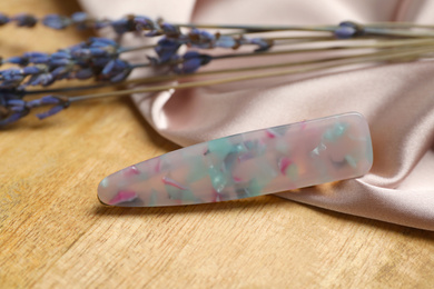 Photo of Stylish hair clip and fabric on wooden table