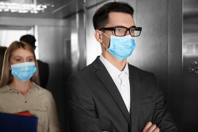 Coworkers with face masks in elevator. Protective measure