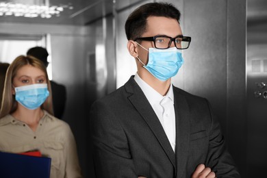 Photo of Coworkers with face masks in elevator. Protective measure