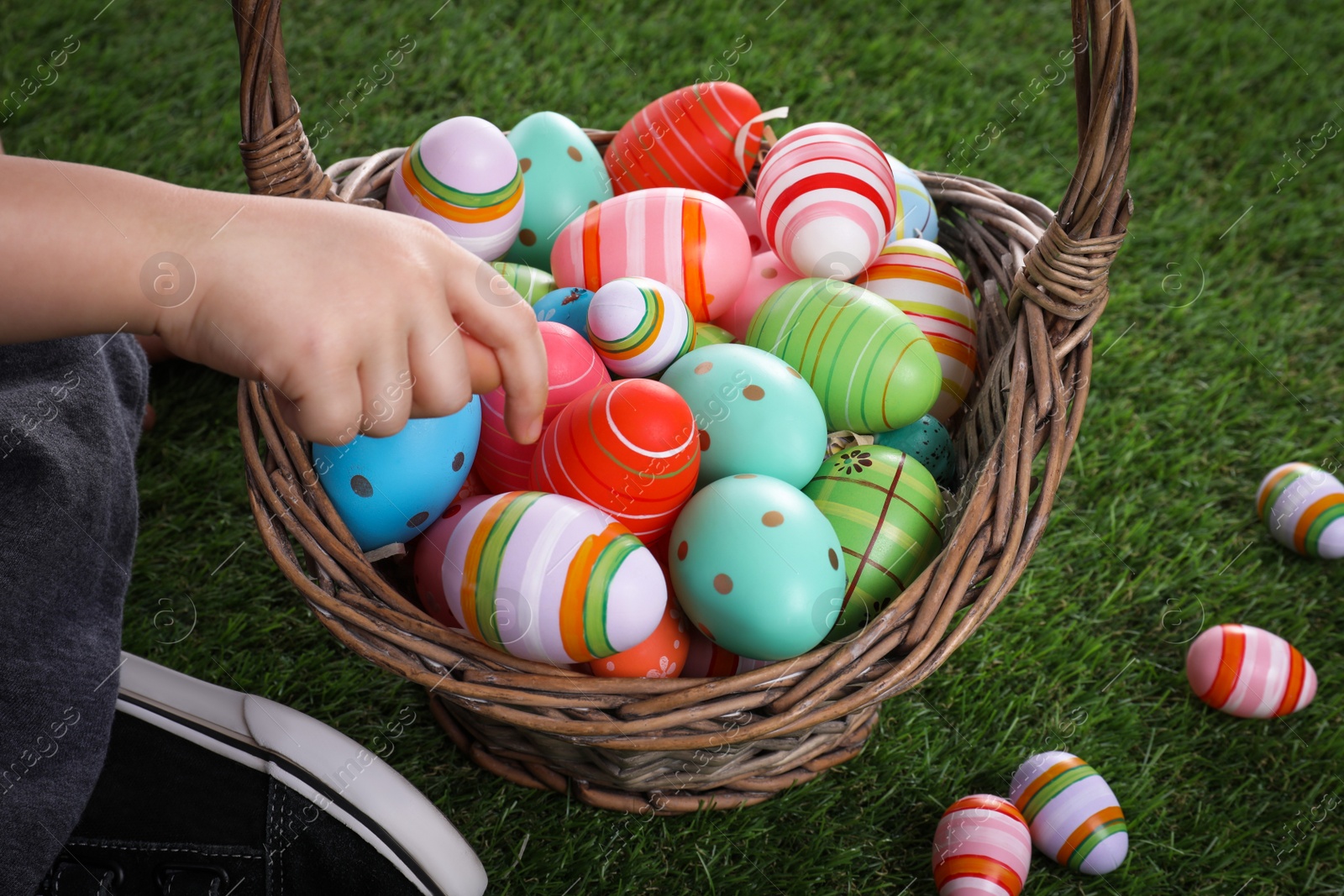 Photo of Little boy with basket full of dyed Easter eggs on green grass, closeup