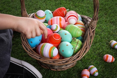 Little boy with basket full of dyed Easter eggs on green grass, closeup