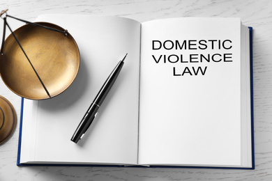 Photo of Domestic violence law and scales of justice on white wooden table, above view