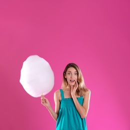 Emotional young woman with cotton candy on pink background