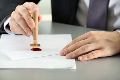 Photo of Male notary sealing document at table, closeup
