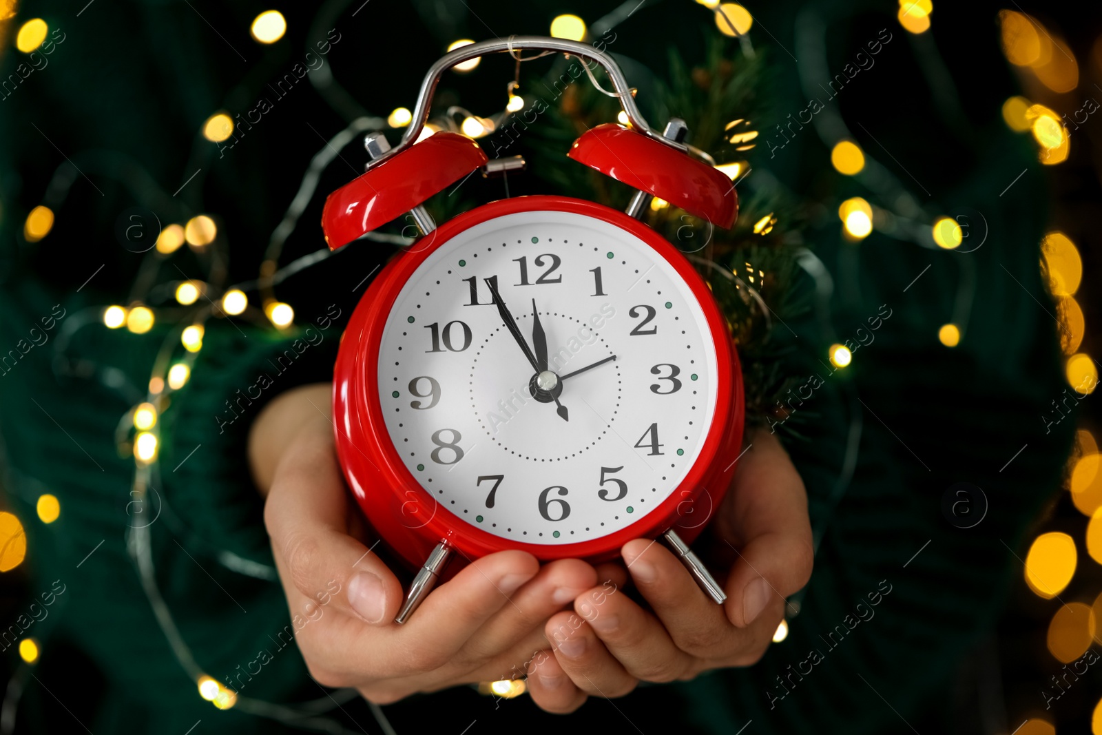 Photo of Woman holding alarm clock against blurred lights, closeup. New Year countdown