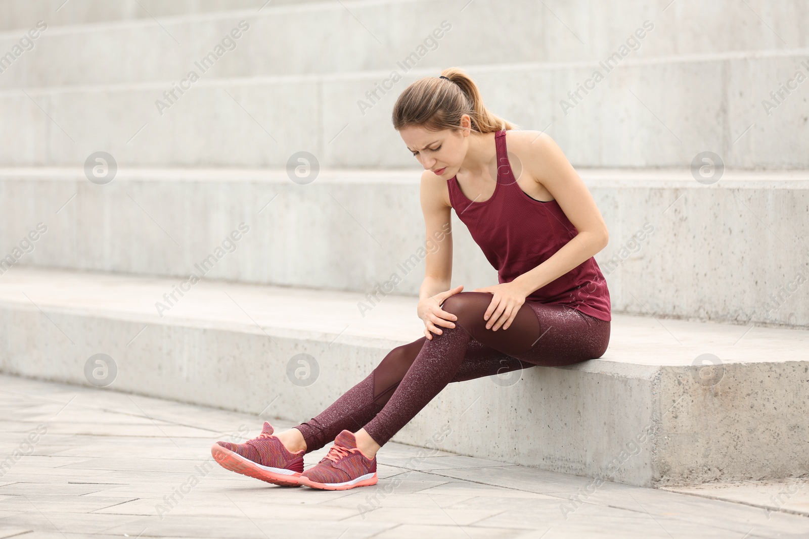 Photo of Woman in sportswear suffering from knee pain on stairs