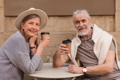 Photo of Affectionate senior couple sitting in outdoor cafe and drinking coffee