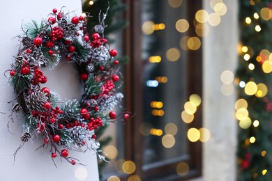 Beautiful Christmas wreath hanging on building wall outdoors, space for text