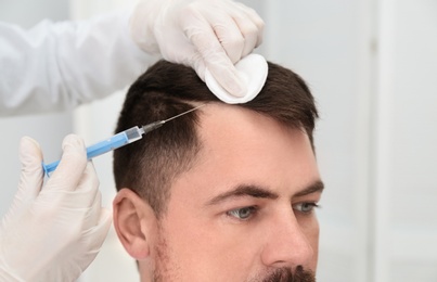 Photo of Man with hair loss problem receiving injection in salon, closeup