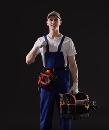 Professional repairman with tool box on black background