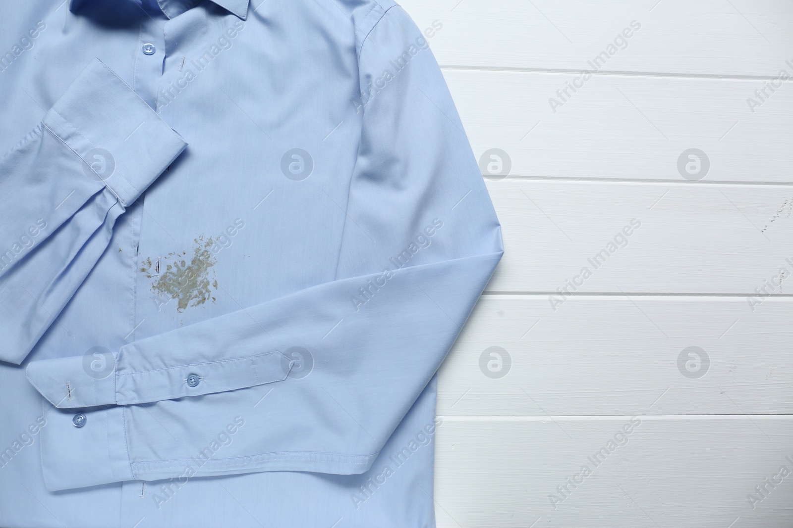 Photo of Light blue shirt with stain on white wooden table, top view. Space for text