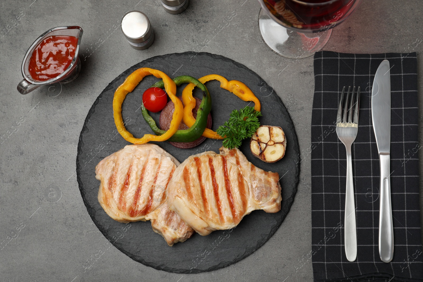 Photo of Grilled meat served with garnish, sauce and wine on grey background, top view