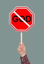 Image of Atheism concept. Man holding prohibition sign with crossed out word God on grey background