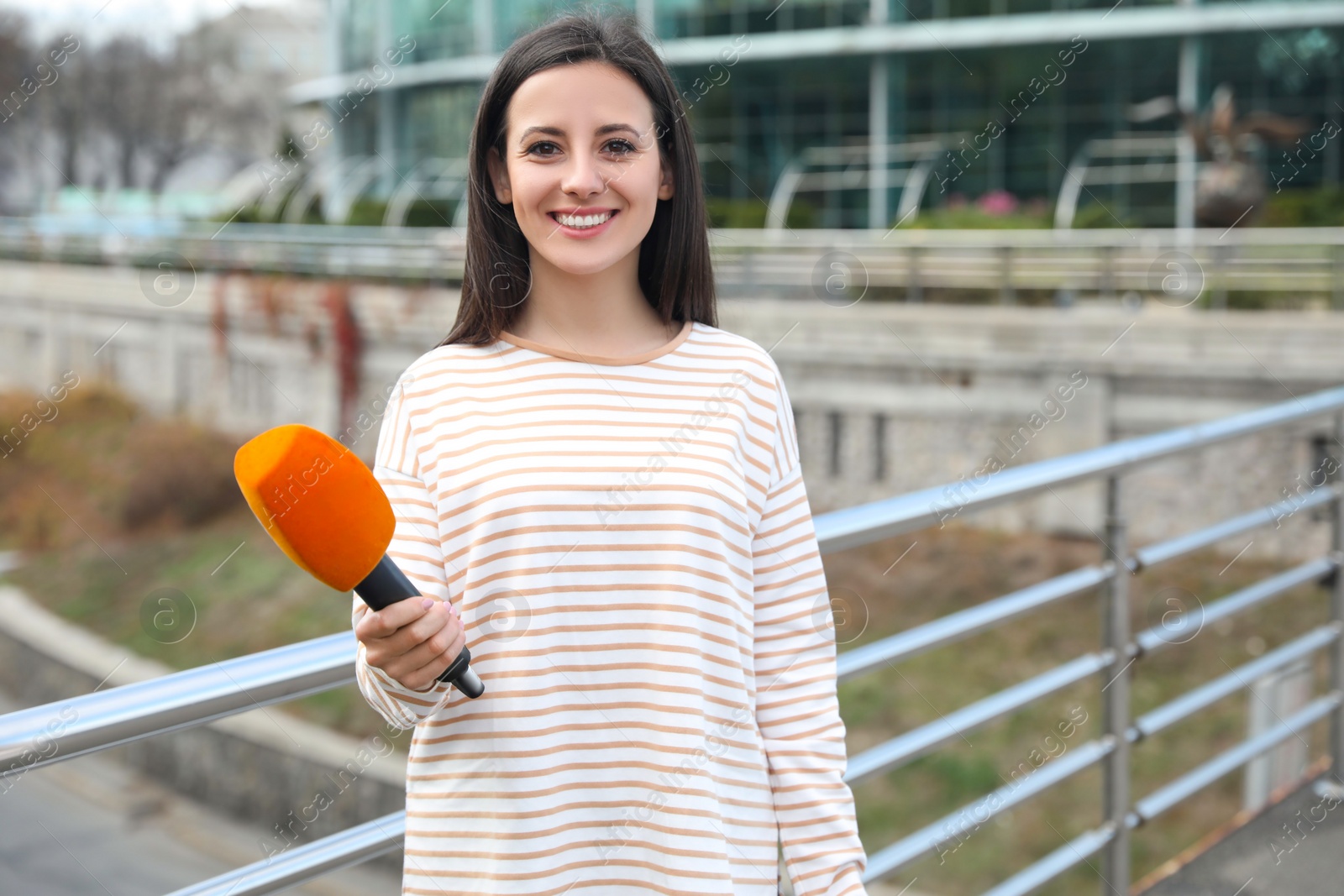 Photo of Young female journalist with microphone working on city street