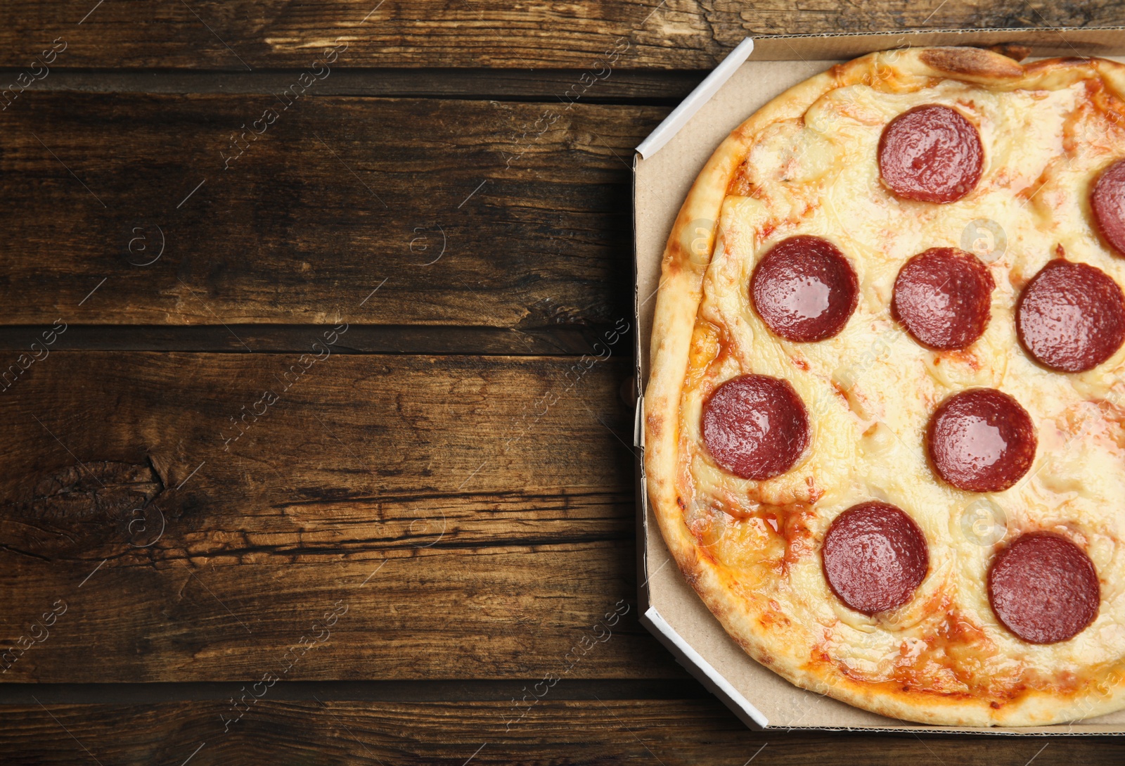 Photo of Tasty pepperoni pizza in cardboard box on wooden table, top view. Space for text