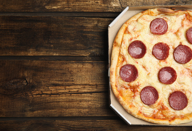 Tasty pepperoni pizza in cardboard box on wooden table, top view. Space for text