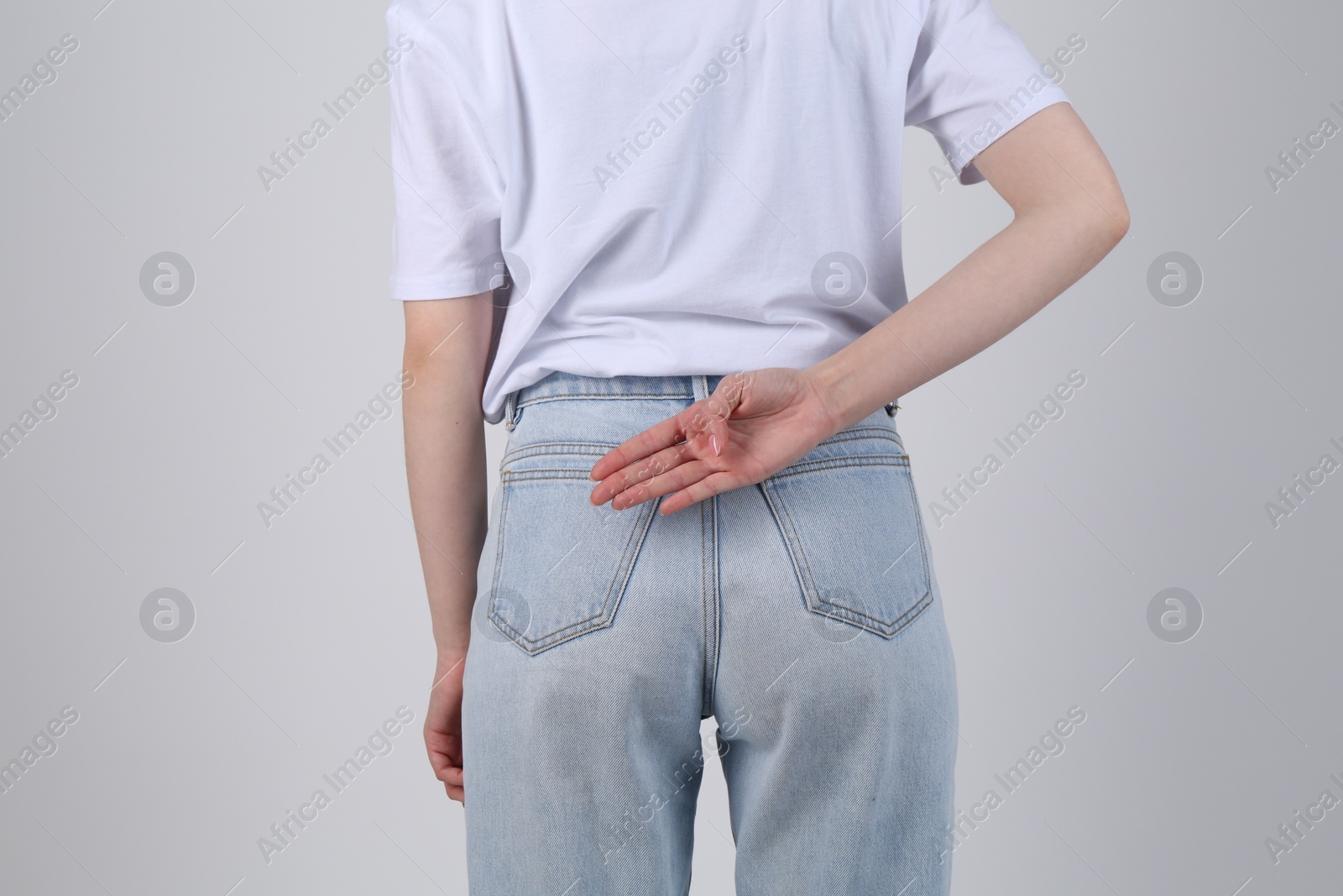 Photo of Woman showing open palm behind her back on light grey background, back view