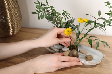 Photo of Woman creating stylish ikebana with beautiful flowers and green branches at table, closeup