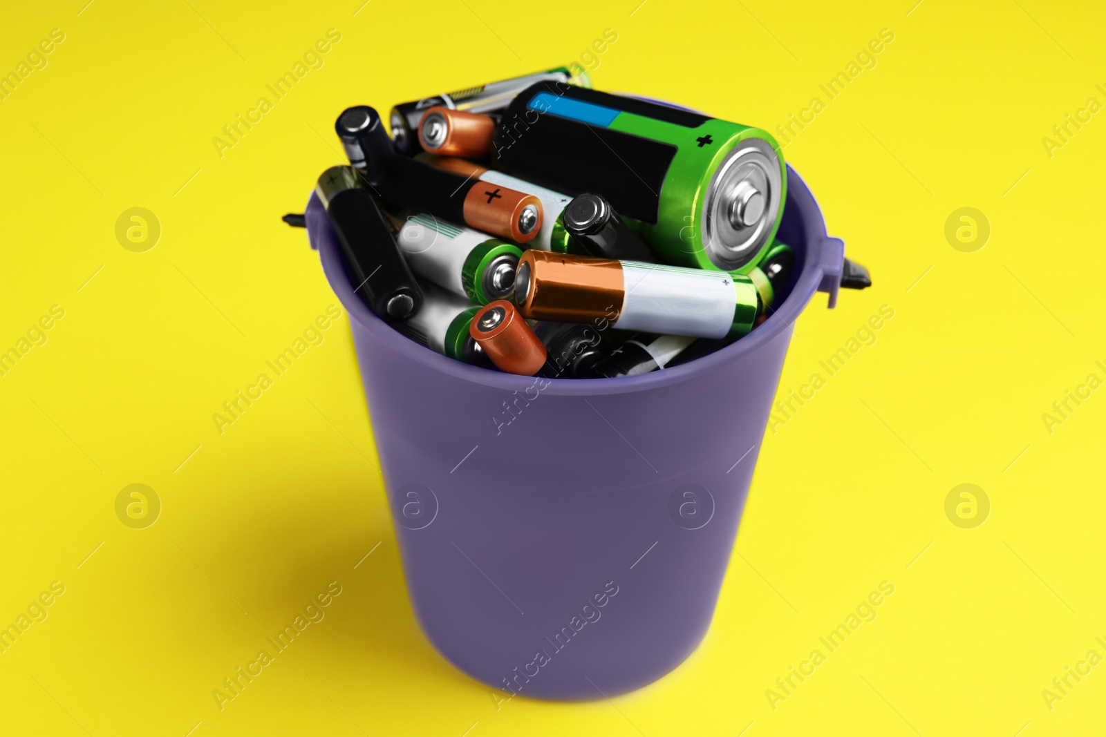 Image of Used batteries in bucket on yellow background, closeup