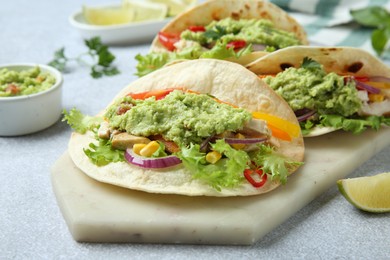 Photo of Delicious tacos with guacamole, meat and vegetables on light grey table, closeup