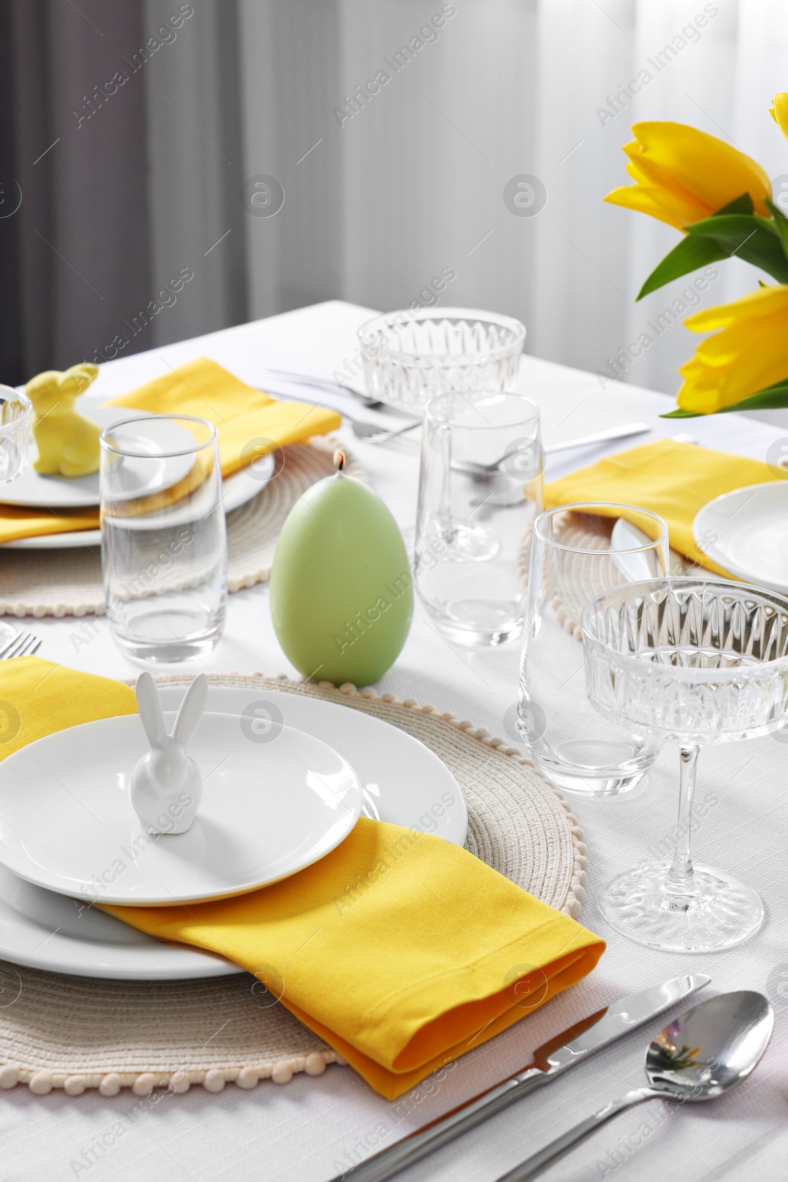 Photo of Festive table setting with glasses, burning candle and vase of tulips. Easter celebration