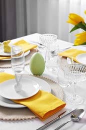 Photo of Festive table setting with glasses, burning candle and vase of tulips. Easter celebration