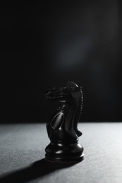Photo of Black knight on table against dark background, space for text. Chess piece