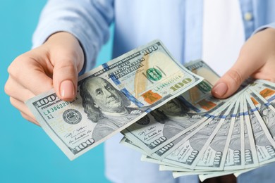 Photo of Woman holding dollar banknotes on turquoise background, closeup. Money exchange concept