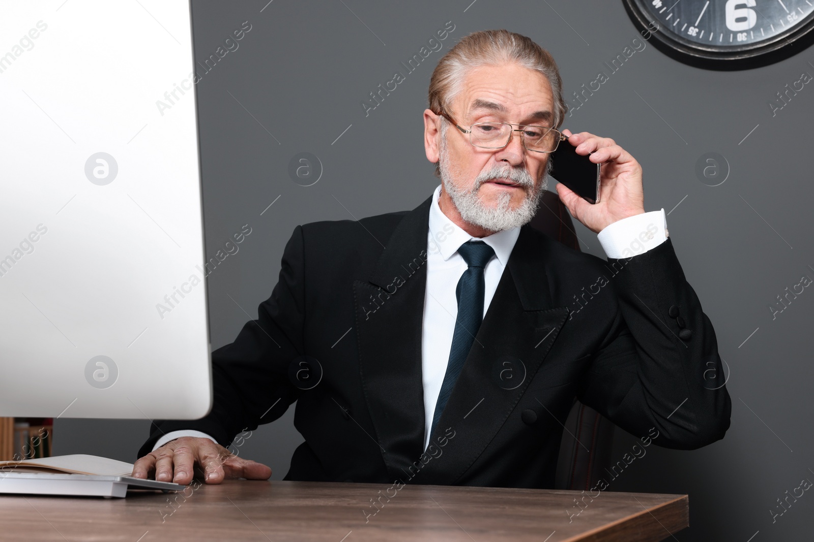 Photo of Senior boss talking on phone at wooden table in office