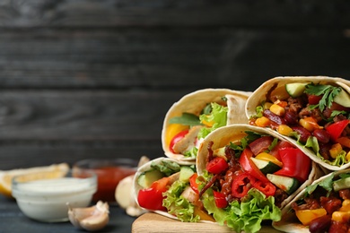 Board with delicious meat tortilla wraps on table against wooden background, closeup. Space for text