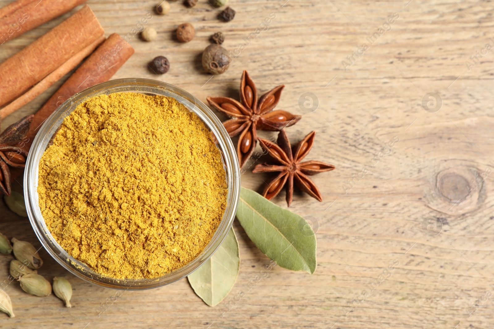 Photo of Curry powder in bowl and other spices on wooden table, flat lay. Space for text