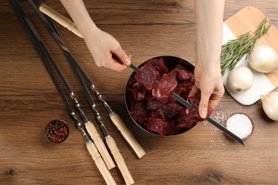 Photo of Woman stringing marinated meat on skewer at wooden table, top view