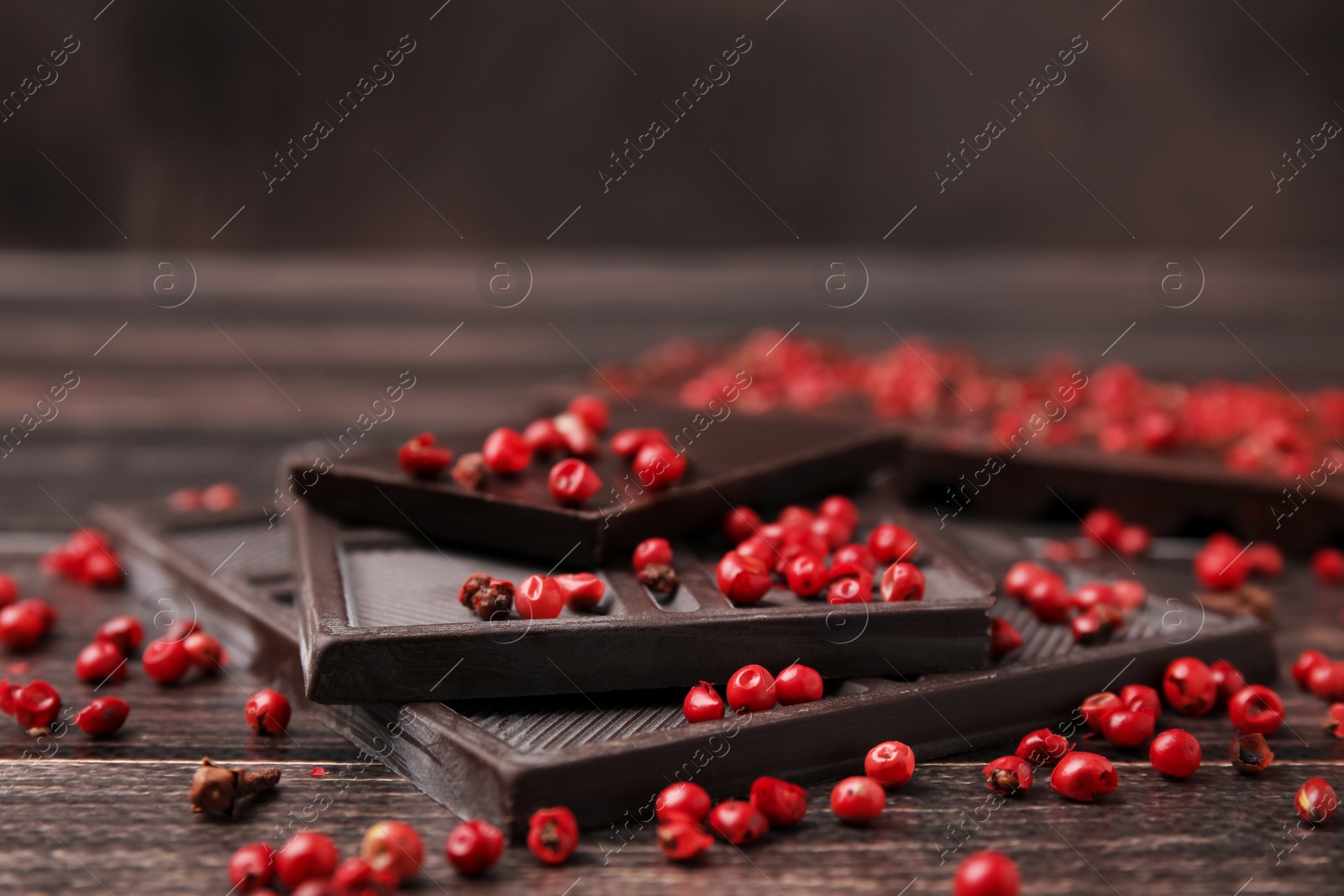 Photo of Delicious chocolate and red peppercorns on wooden table, closeup