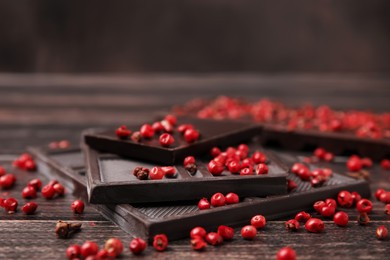 Delicious chocolate and red peppercorns on wooden table, closeup