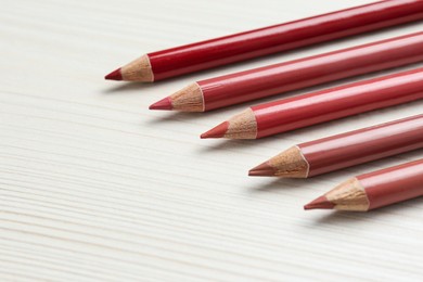 Many lip pencils on white wooden table, space for text