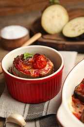Photo of Baked eggplant with tomatoes, cheese and basil in ramekin on table