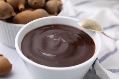 Photo of Bowl of tamarind sauce, spoon and fresh pods on table, closeup
