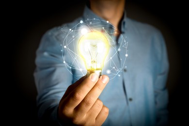 Image of Glow up your ideas. Man holding light bulb on black background, closeup