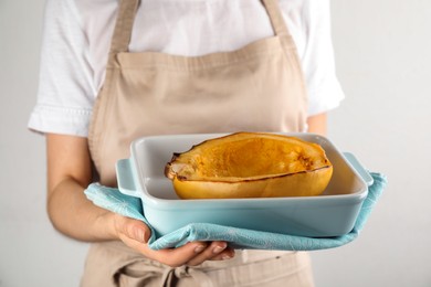 Photo of Woman holding baking dish with half of cooked spaghetti squash on light background, closeup