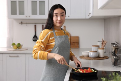 Photo of Beautiful woman cooking vegetable dish in kitchen
