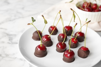 Photo of Plate of chocolate dipped cherries on white marble table