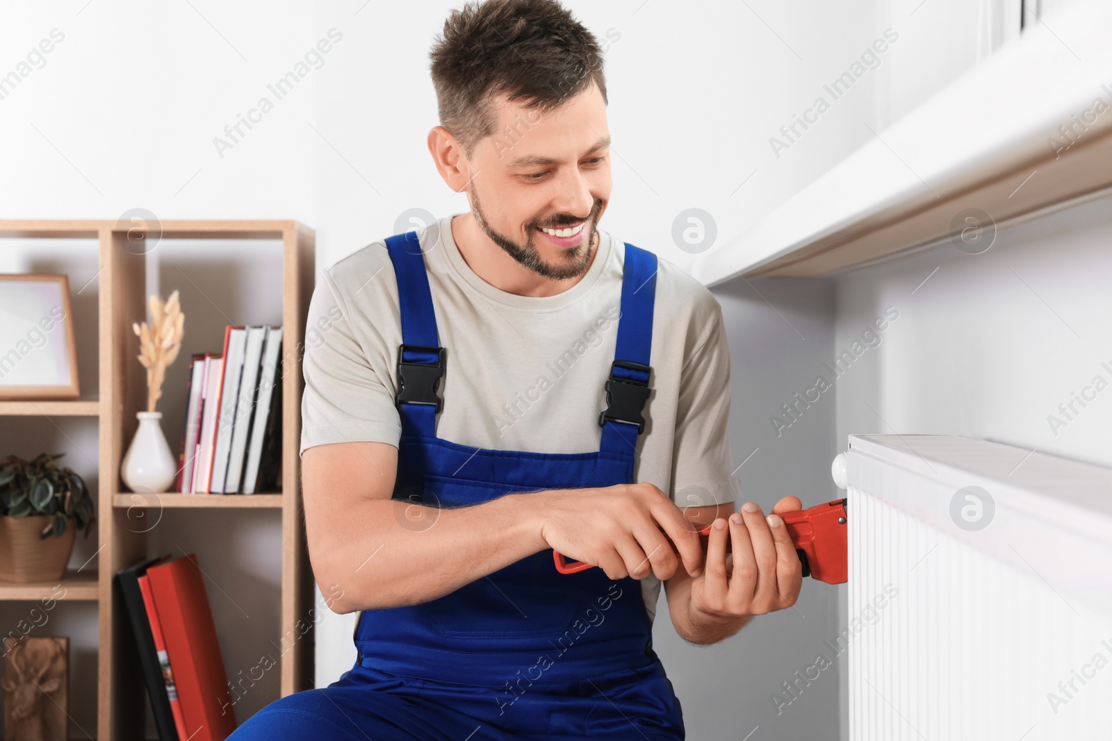 Photo of Professional plumber using adjustable wrench for installing new heating radiator in room