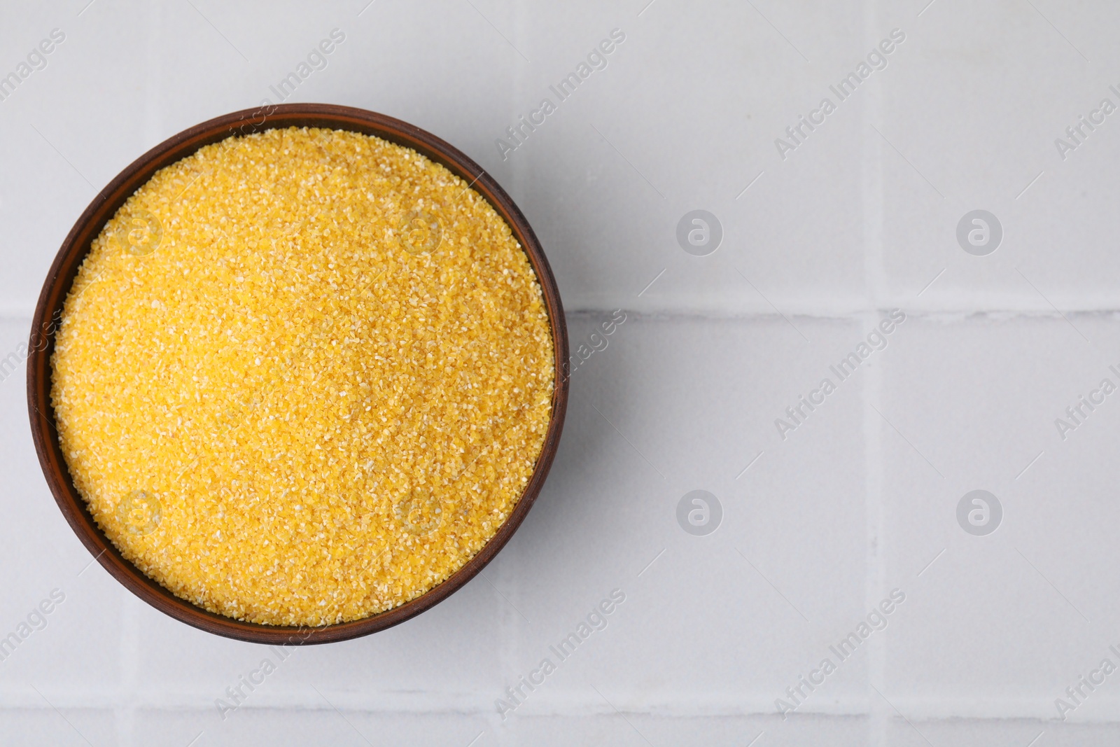 Photo of Raw cornmeal in bowl on white tiled table, top view. Space for text