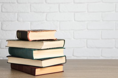 Photo of Stack of old hardcover books on wooden table near white brick wall, space for text
