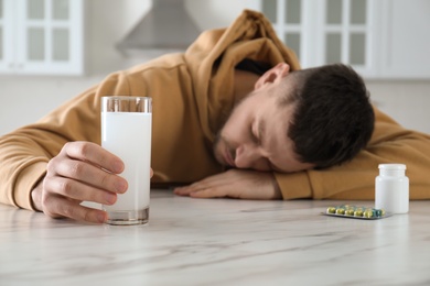 Photo of Man sleeping at table in kitchen, focus on hand with glass of medicine for hangover
