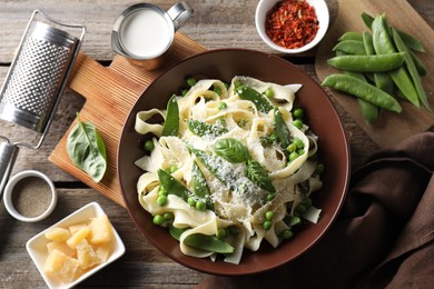 Photo of Delicious pasta with green peas and ingredients on wooden table, flat lay