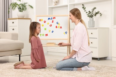 Mom teaching her daughter alphabet with magnetic letters at home