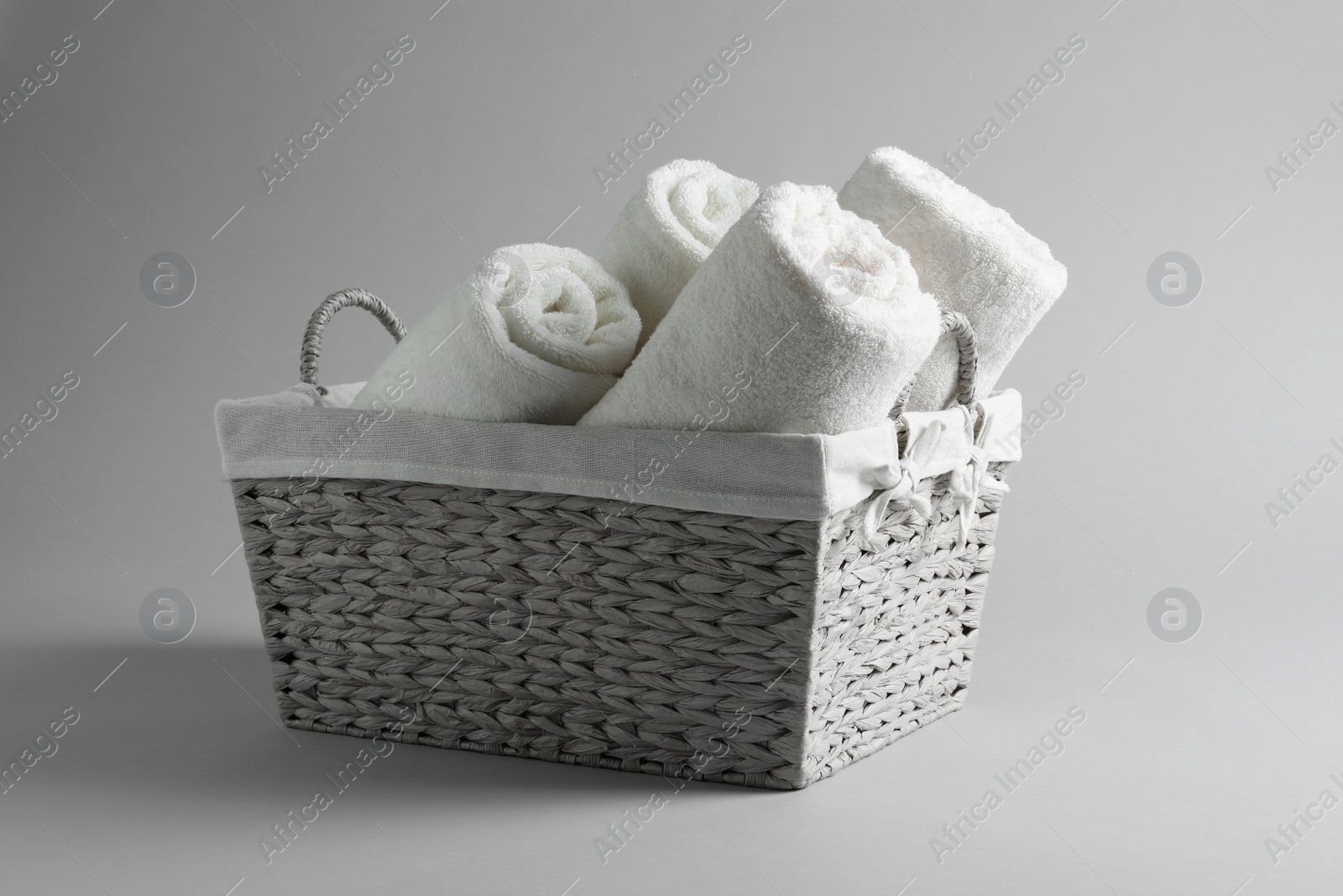 Photo of Basket with rolled towels on light background